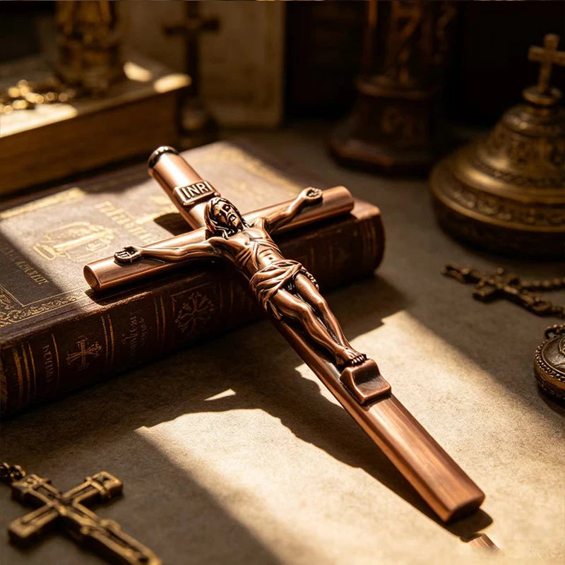 A bronze crucifix pen set featuring an INRI Jesus cross writing instrument resting on a leather-bound book.