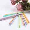 A collection of colorful plastic crochet hooks in various sizes, laid out next to pink and green tulips.