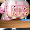 A pink interactive remote-controlled robot with large eyes and a control panel is shown on a wooden surface.