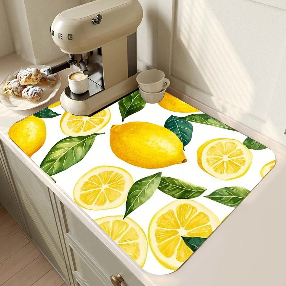 A yellow and green lemon print absorbent kitchen drying mat placed on a countertop next to a coffee machine.