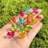A hand holds ten colorful glitter resin duck figurines in various shades of pink, green, and yellow.