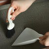 A hand is holding a white compact mini broom and dustpan set on a dark surface.