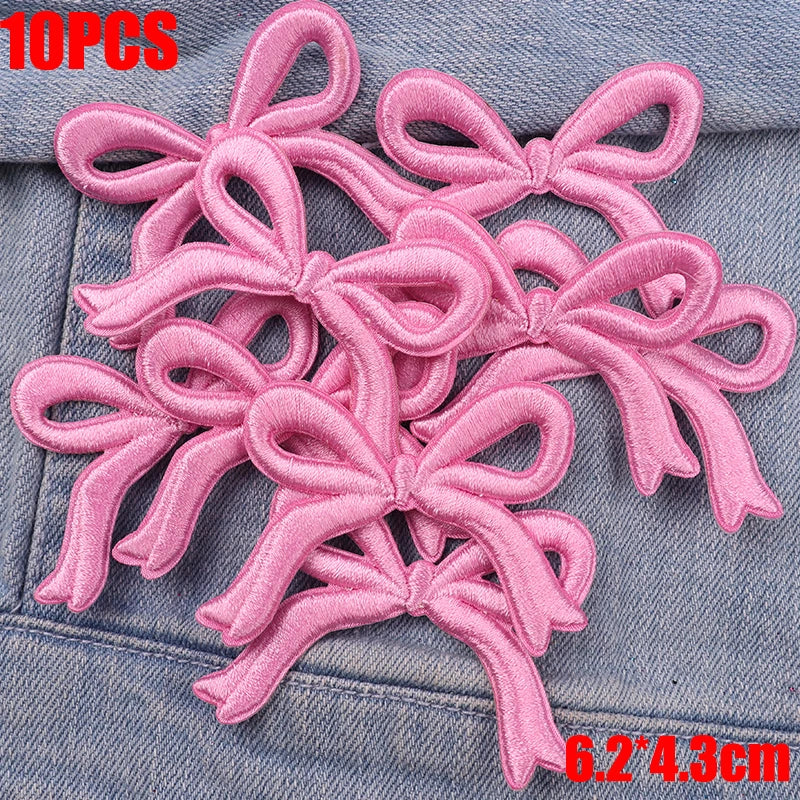 Ten pink embroidered cartoon bow iron-on patches scattered on a denim fabric.