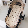 A beige baby stroller seat cushion with padded support and a patterned fabric is shown on a stroller frame.