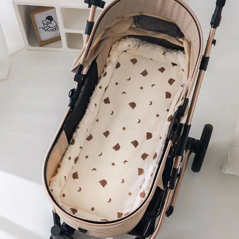 A beige baby stroller seat cushion with padded support and a patterned fabric is shown on a stroller frame.