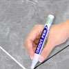 A hand holds a purple tile sewing pen applying grout to a gray tiled surface.