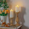 A set of LED pillar candles in a golden tone displayed on a wooden surface with greenery.