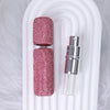 A pink textured glass perfume atomizer refill with a silver cap displayed in a white holder.