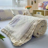 A rolled floral washed cotton gauze summer quilt with light gray and white tones.
