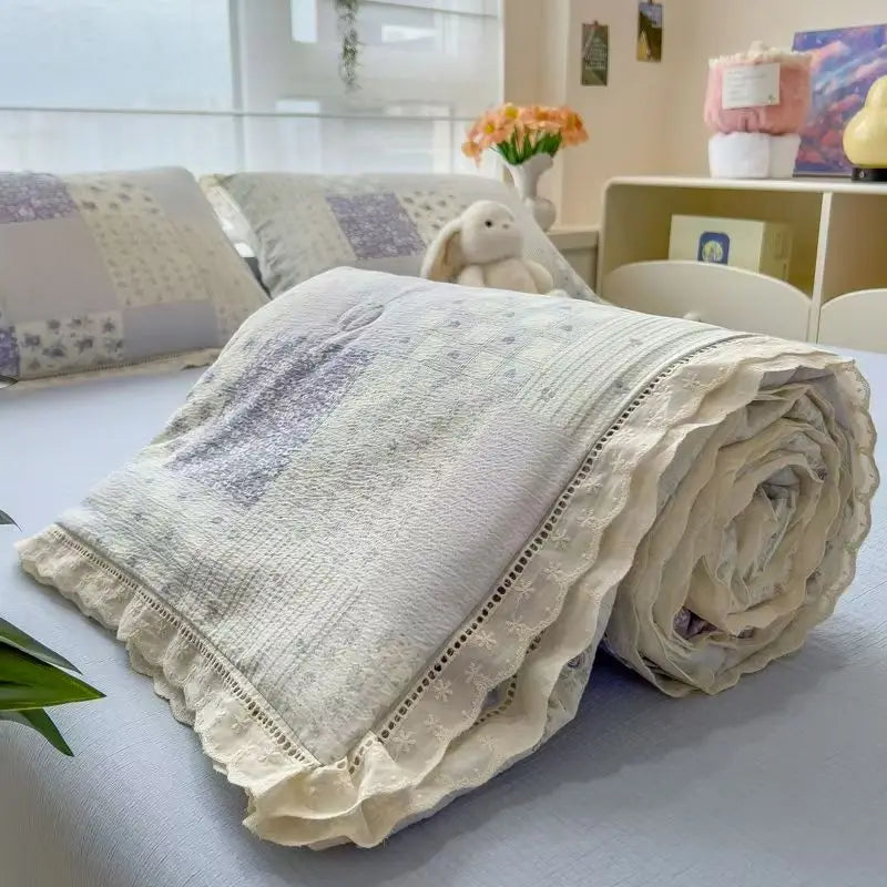 A rolled floral washed cotton gauze summer quilt with light gray and white tones.