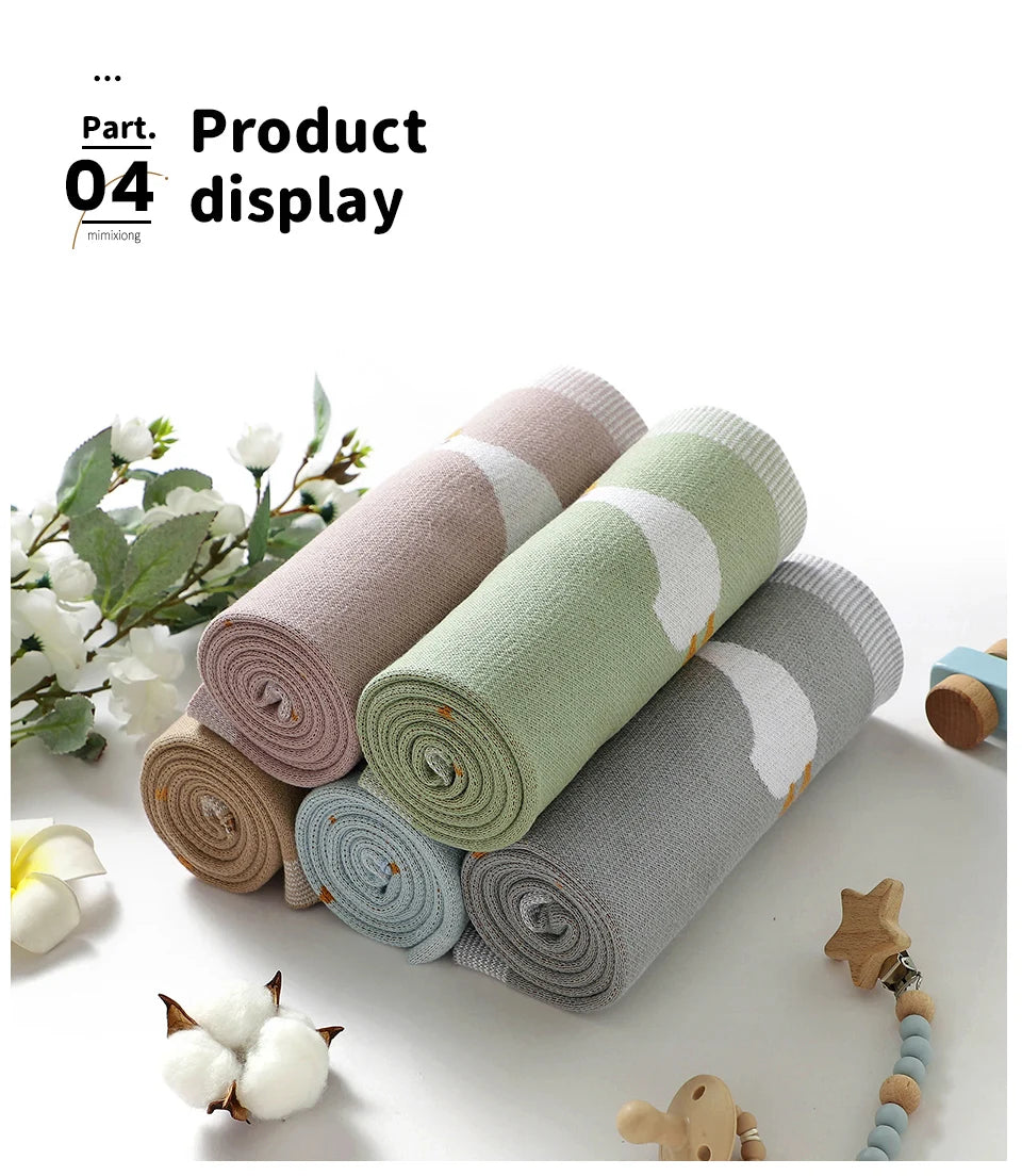 Rolls of soft cotton baby swaddle blankets in pastel colors with white cartoon prints displayed on a white surface.