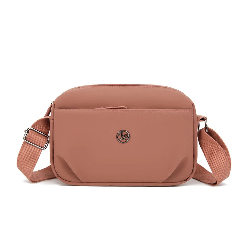 A light dusty rose nylon crossbody bag with a flap closure and leather strap.