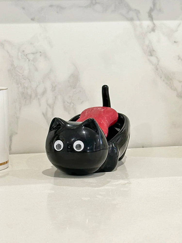 A black cat-shaped soap box with a red drainage tray sits on a white countertop.