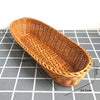 A long, oval handwoven wicker serving basket in natural brown color shown on a checkered surface.