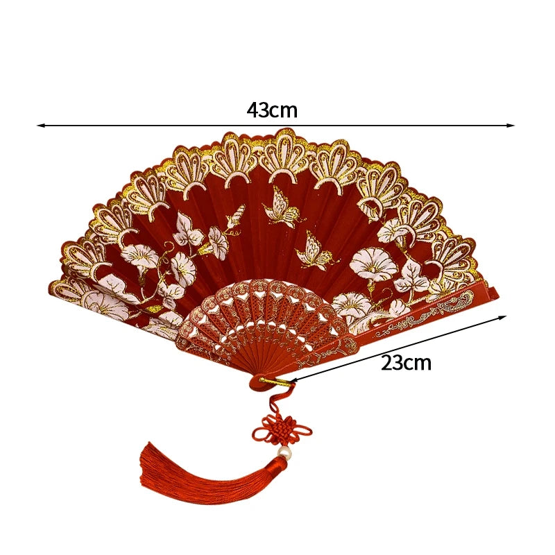 A vintage folding fan with a deep red fabric and golden lace trim, shown open.