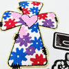 An embroidered cross patch featuring red, blue, and purple flowers on a white background.