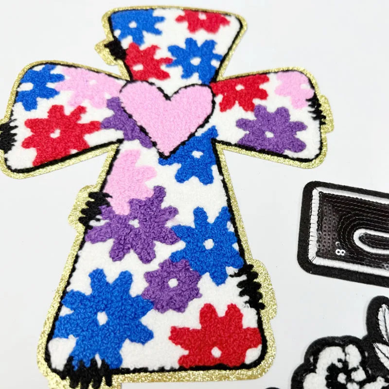 An embroidered cross patch featuring red, blue, and purple flowers on a white background.