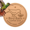 A copper disk bird bath cleaner with a silhouette of a bird on it, used for garden water.