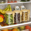 A row of airtight glass storage jars with bamboo lids and spoons filled with various dried fruits and vegetables.