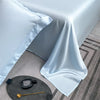 A folded light blue silk sheet draped on a table, next to a gold measuring tool.