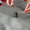 Hands are adjusting a gray plush winter car seat cover with a red trim on a vehicle seat.