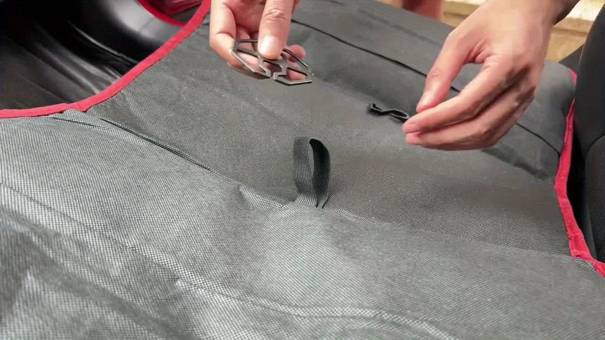 Hands are adjusting a gray plush winter car seat cover with a red trim on a vehicle seat.