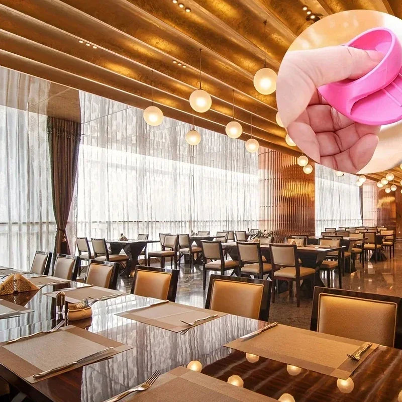 A hand wearing pink silicone finger covers is shown against a backdrop of modern dining tables and lighting.