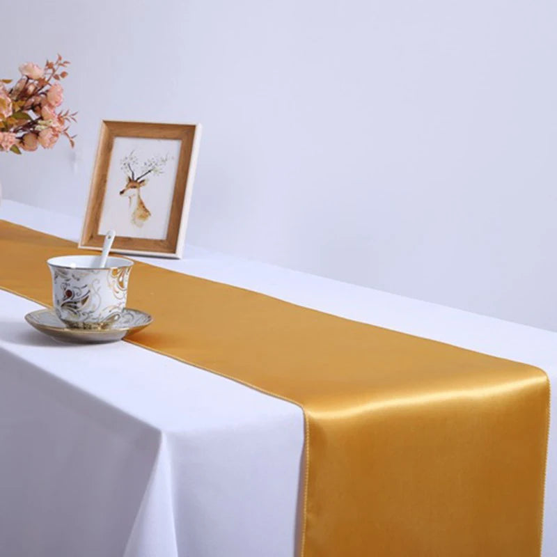 Elegant satin gold table runner on a white tablecloth with a framed picture and teacup.