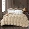 A beige quilted comforter with white pillows is displayed on a bed in a softly lit room.