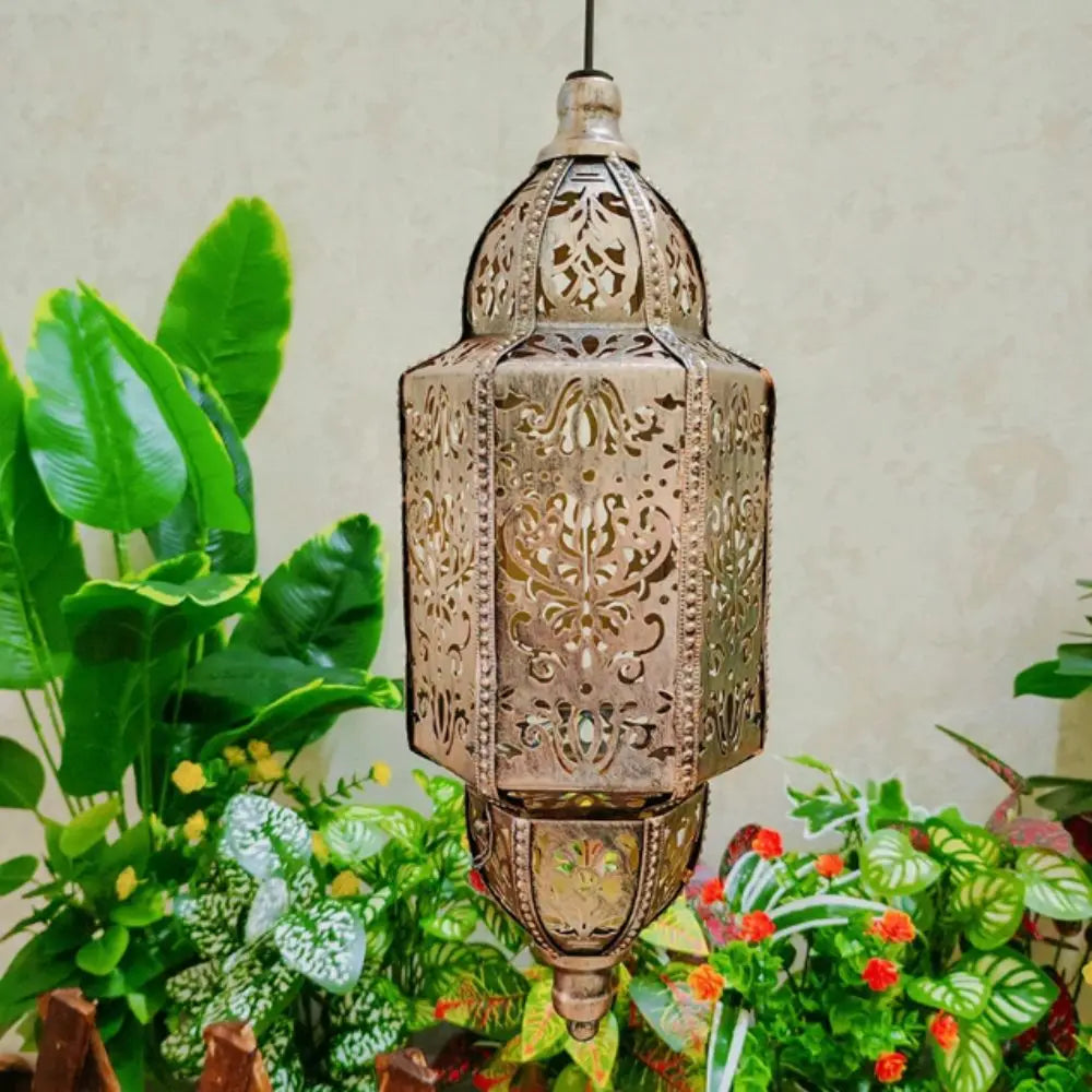 A bronze solar-powered Moroccan lantern with intricate ironwork hanging above lush green foliage.