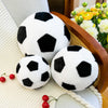 A white and black realistic football plush pillow resting on a cream-colored surface next to a woven basket.