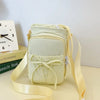 A light cream crossbody bag with a bow detail and adjustable strap resting on a surface.