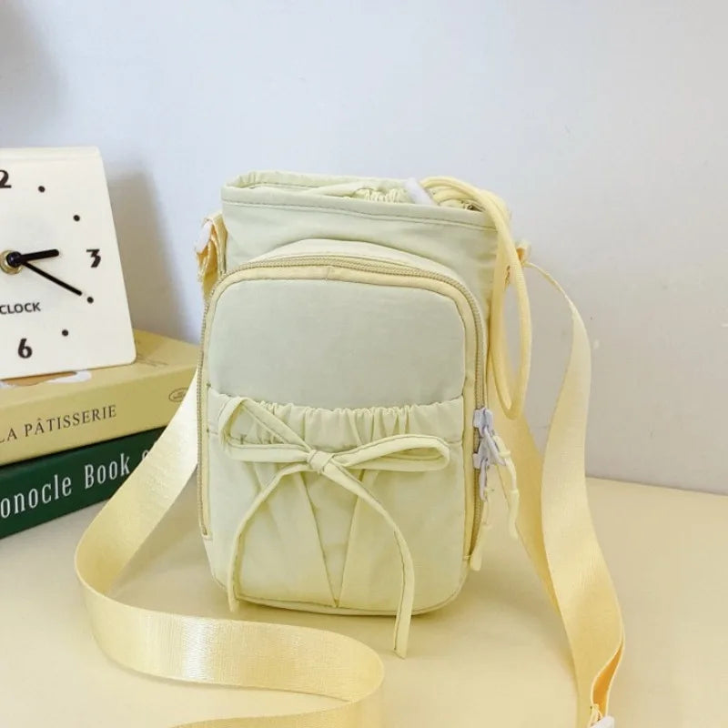 A light cream crossbody bag with a bow detail and adjustable strap resting on a surface.