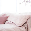 A close-up of a soft pink linen pillowcase with a textured cover and envelope closure on a bed.