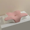 A pink ergonomic memory foam cervical pillow with a white textured cover is shown on a light surface.