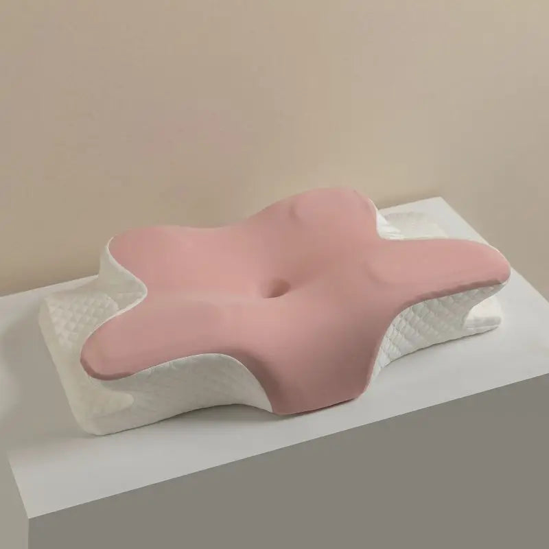 A pink ergonomic memory foam cervical pillow with a white textured cover is shown on a light surface.