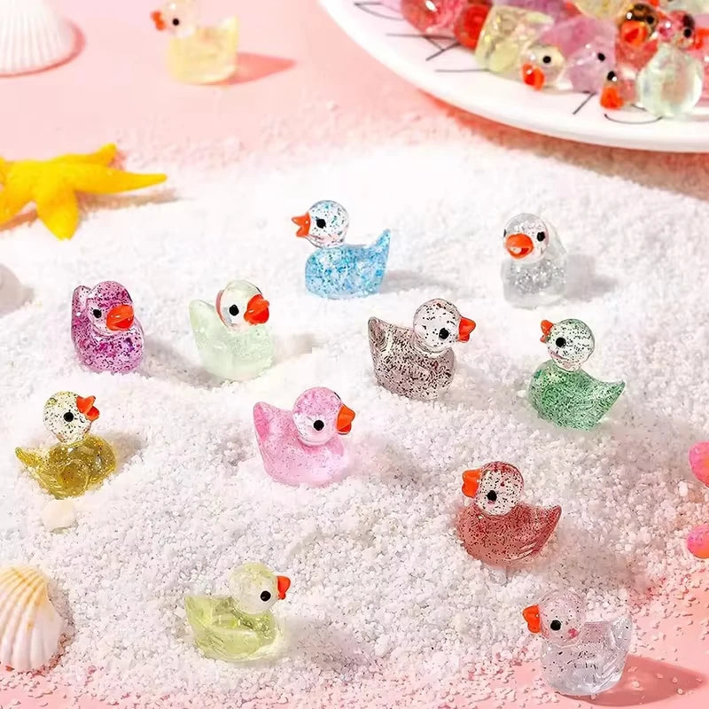 A collection of ten glitter resin duck figurines scattered on pink snow-like powder.