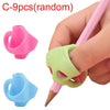 A hand holds a pink pencil with a green grip trainer, showing two different colored silicone grips for posture correction.