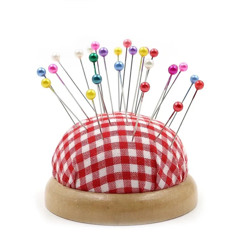 A collection of colorful round pearl straight pins arranged on a red and white checkered fabric base.