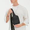 A male model holds a black 2-in-1 convertible waist and crossbody sling bag against a white t-shirt.