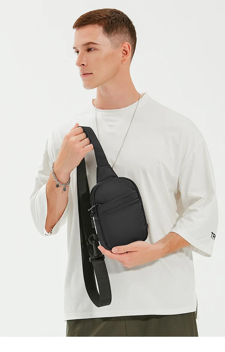 A male model holds a black 2-in-1 convertible waist and crossbody sling bag against a white t-shirt.