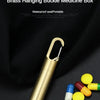 A brass hanging buckle medicine box with a keychain is shown next to several yellow and red pills.