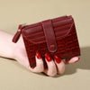 A close-up of a maroon PU leather wallet with a textured pattern and a flap closure being held by a hand.