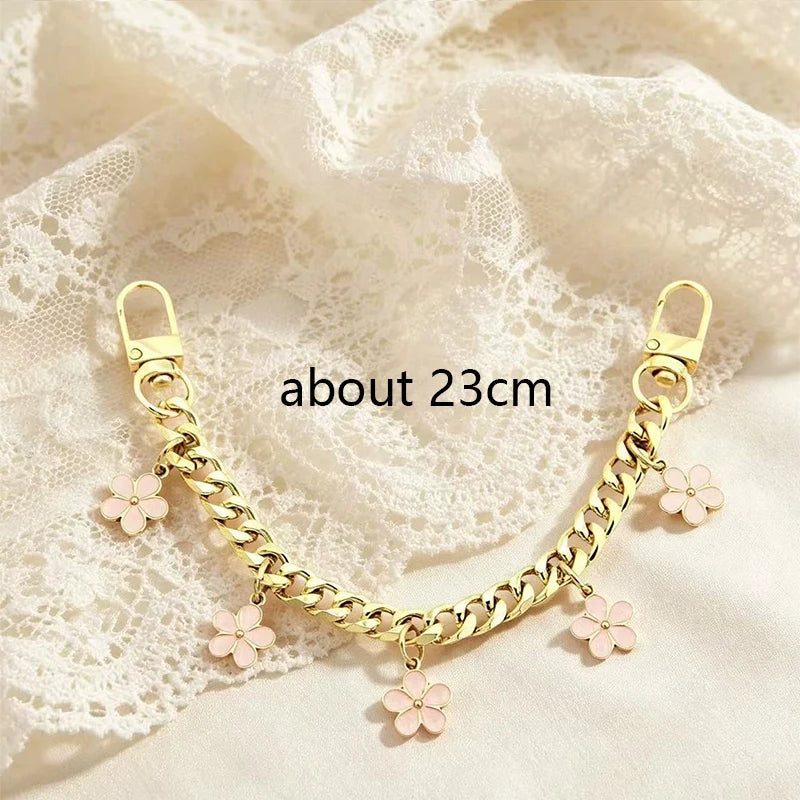 A gold-colored chain necklace featuring small pink flower charms draped on a sheer white fabric.