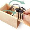A wooden box contains a trick toy featuring a spider and a small insect, with green arrows indicating movement.