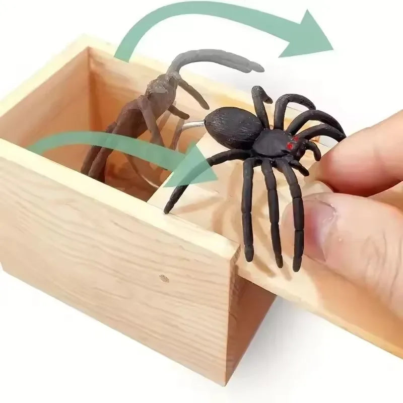 A wooden box contains a trick toy featuring a spider and a small insect, with green arrows indicating movement.