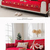 A red Christmas tree patterned sofa cover displayed on a white sofa with a gold-colored fluffy decoration.