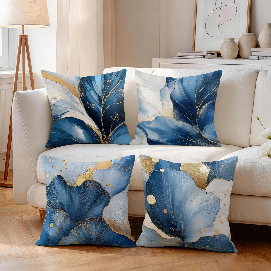 A set of abstract leaf print cushion covers in shades of blue and gold on a white sofa.