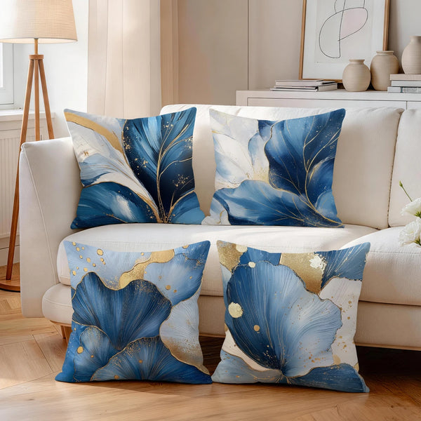 A set of abstract leaf print cushion covers in shades of blue and gold on a white sofa.
