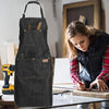 A dark gray multi-pocket denim and waxed canvas work apron hanging on a wooden surface.